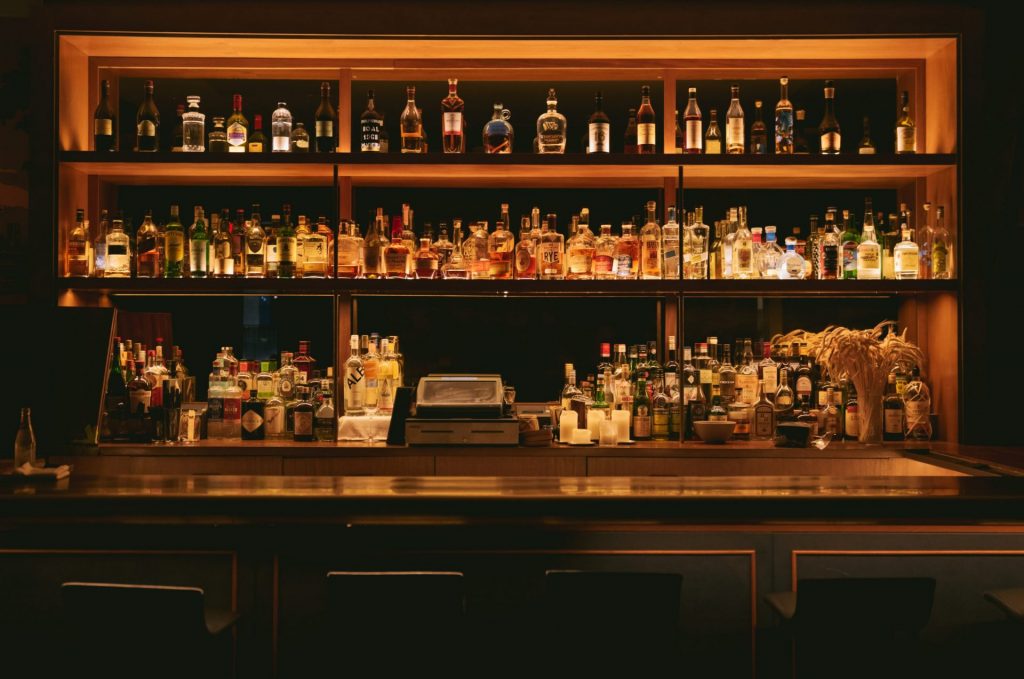 A wooden shelf with a dim, yellow light overhead and bottles of alcoholic drink inside.